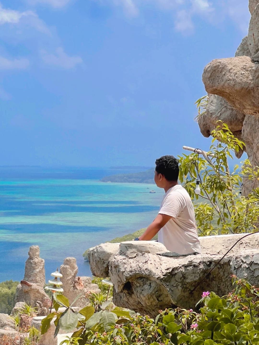Farrel duduk di tebing menghadap laut biru
